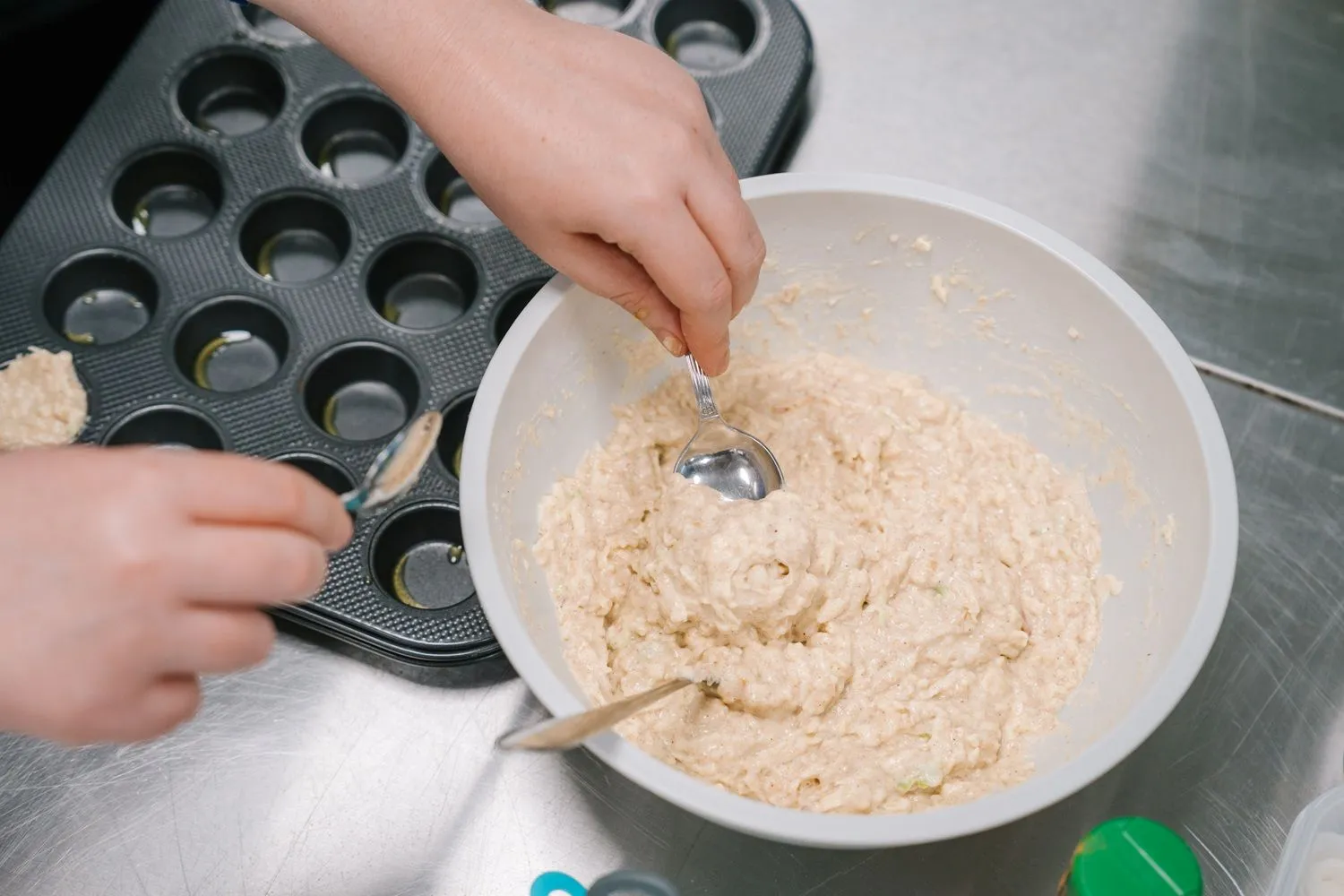 Muffin mixture in bowl being scooped with teaspoons into muffin tray.